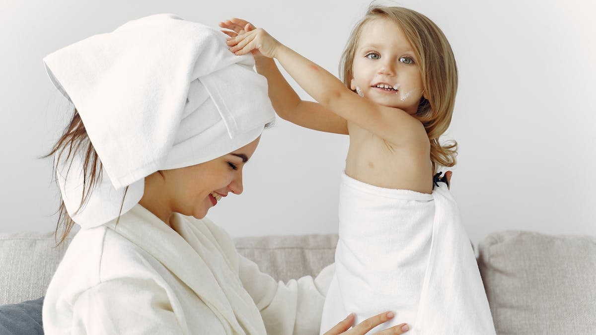 Joyful mother and daughter bonding indoors with towels wrapped around them.